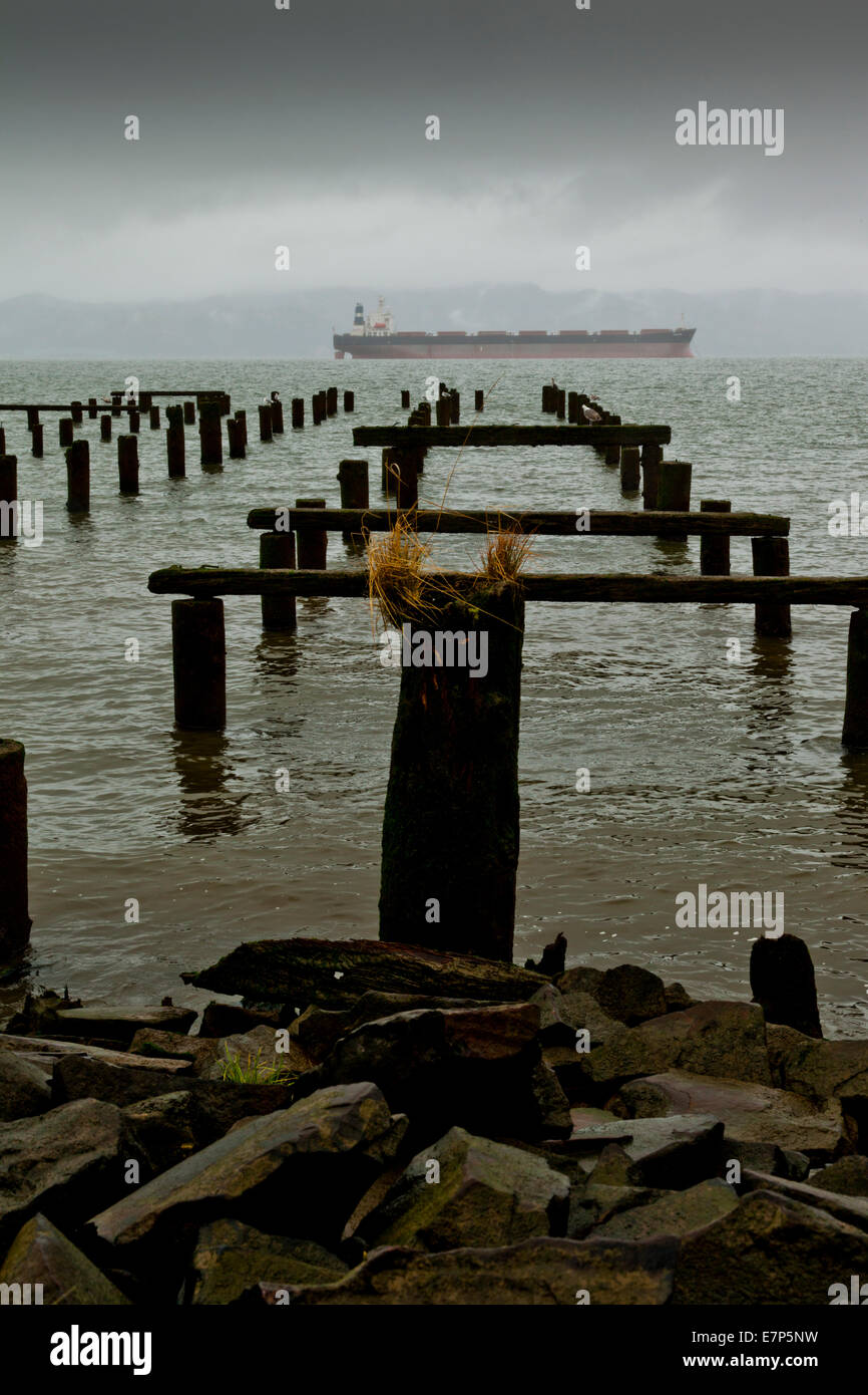 Holzpfähle ragen aus dem Columbia River, während ein Tanker von im Hintergrund dampft Stockfoto