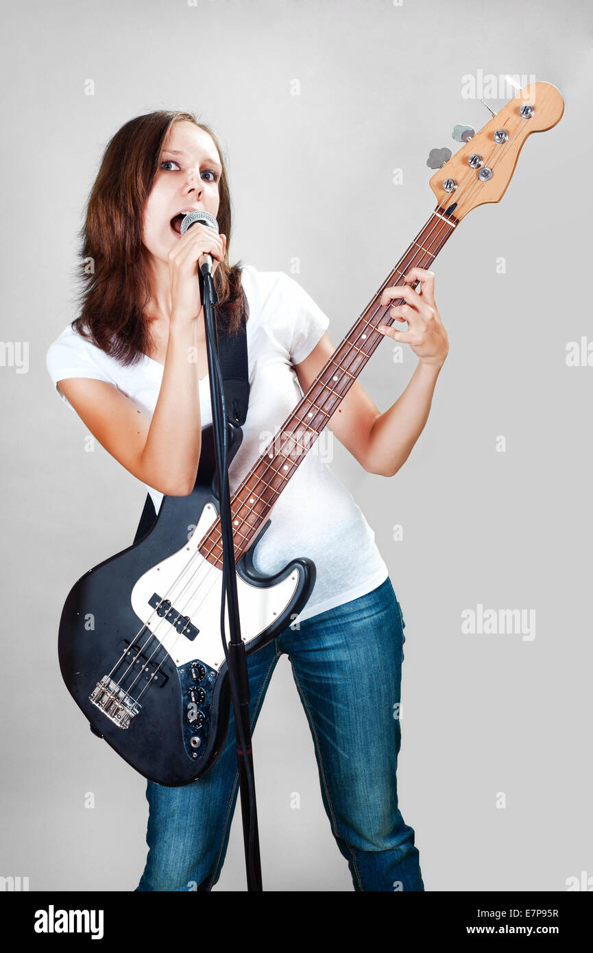 Mädchen mit Gitarre und Mikrofon auf grauem Hintergrund isoliert Stockfoto