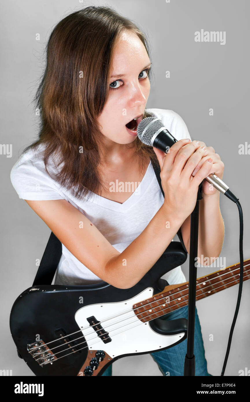 Mädchen mit Gitarre und Mikrofon auf grauem Hintergrund isoliert Stockfoto