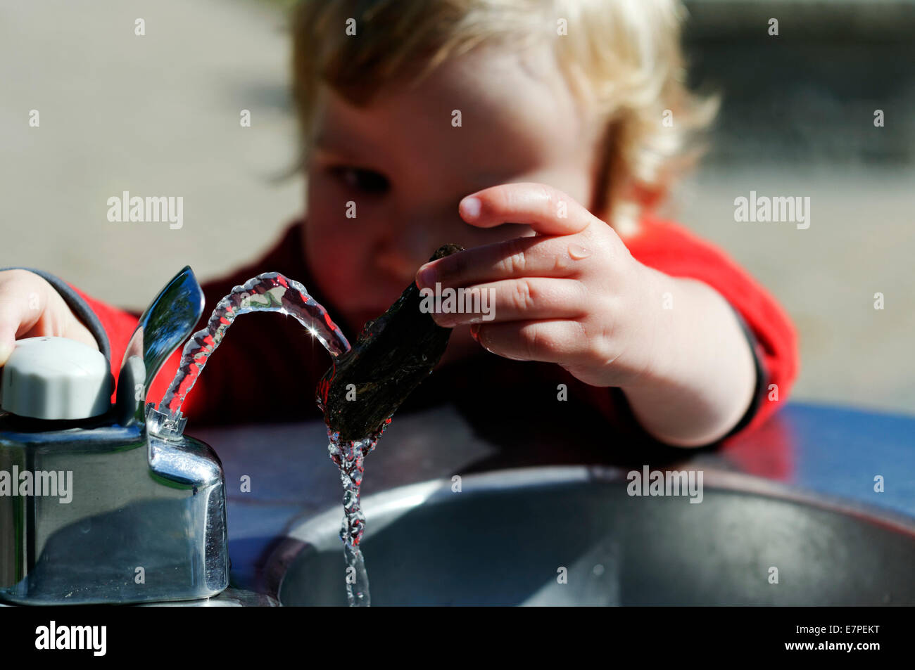Ein kleiner Junge (2 1/2 Jahre alt) spielen mit einem Wasserbrunnen Stockfoto