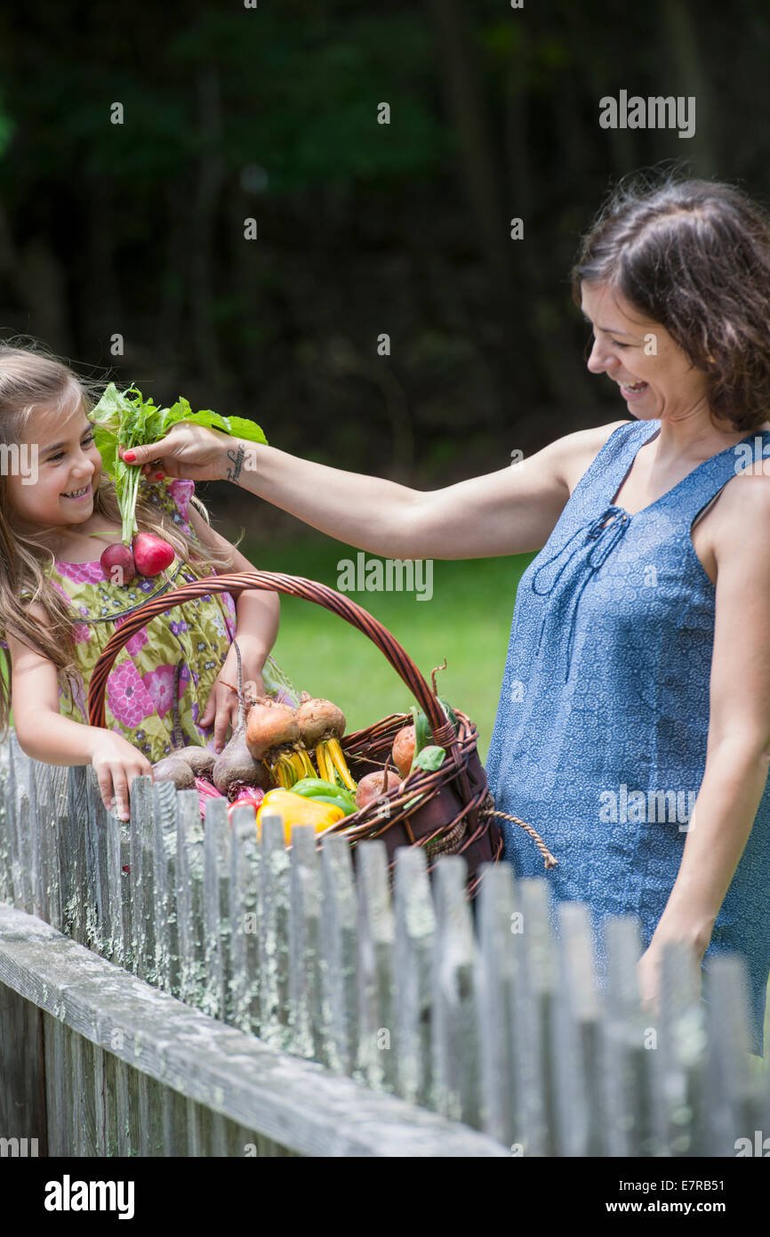 Mutter und Tochter stehen in einem Garten mit einem Korb voller Gemüse. Stockfoto