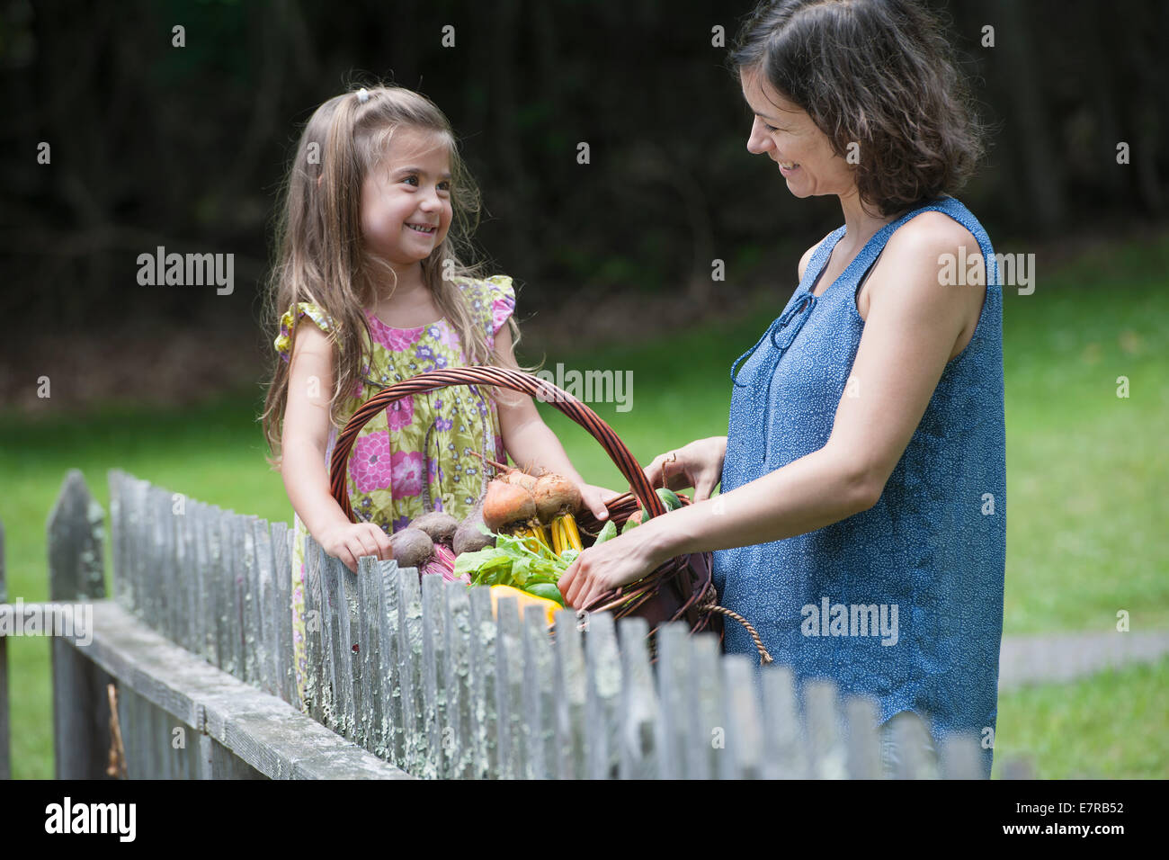 Mutter und Tochter stehen in einem Garten mit einem Korb voller Gemüse. Stockfoto