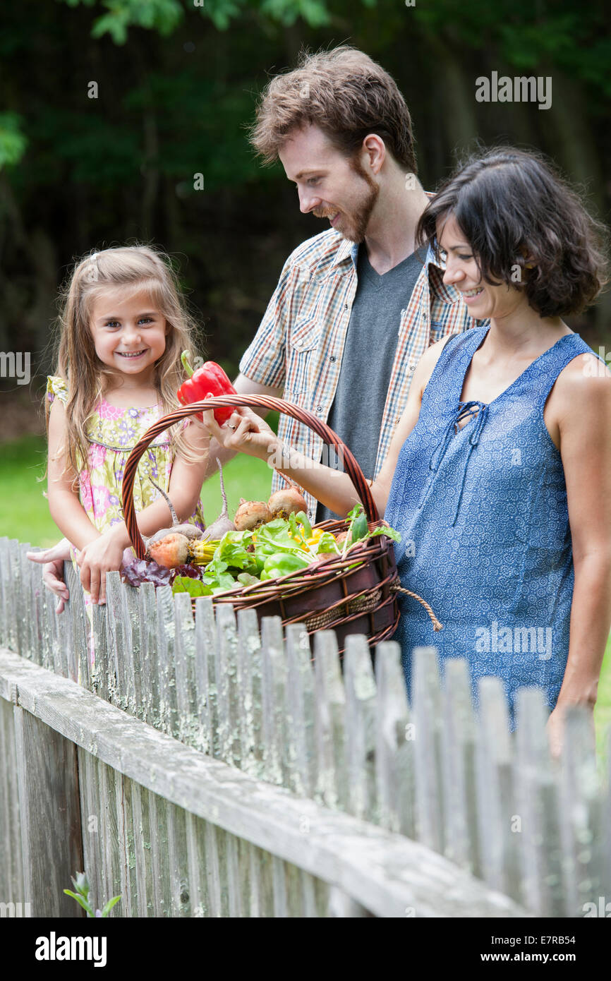 Familie steht in einem Garten mit einem Korb voller Gemüse. Stockfoto