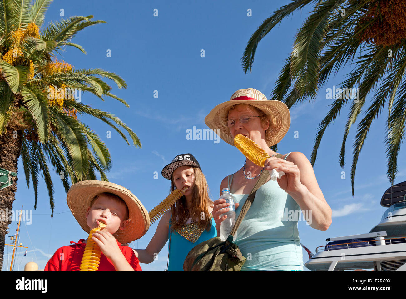 Mutter und Kinder freuen sich über frittierte Kartoffeln vor einer Yacht an der Uferpromenade von Trogir, Dalmatien, Kroatien Stockfoto
