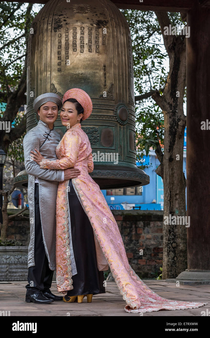 Bräutigam in grau, rosa Ao Dai Braut mit Bronzeglocke Hintergrund. Stockfoto