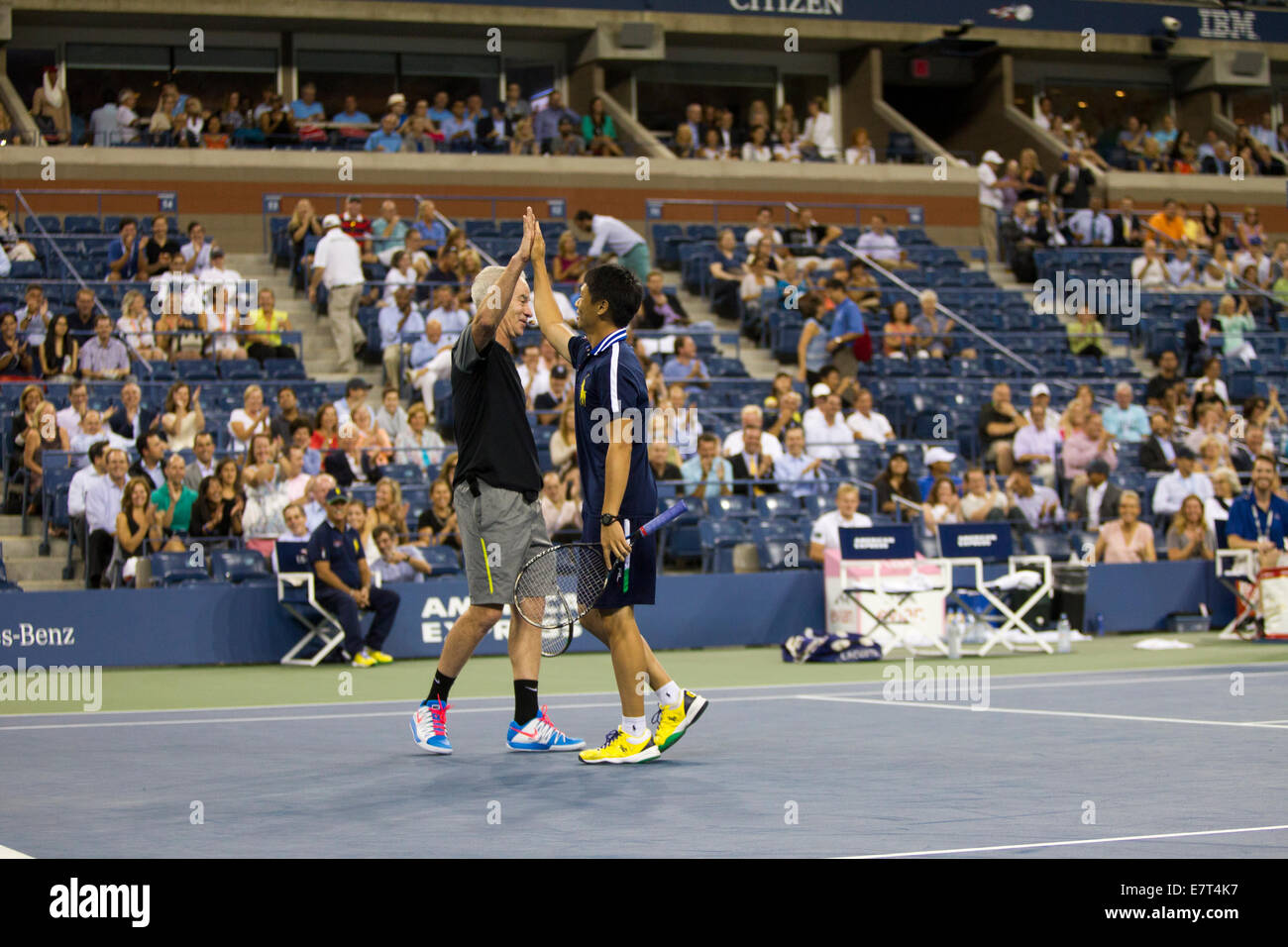 John McEnroe (USA) high Fives Balljunge während einer Ausstellung match bei den 2014 US Open Tennis Championships. © Paul J. Sutton Stockfoto