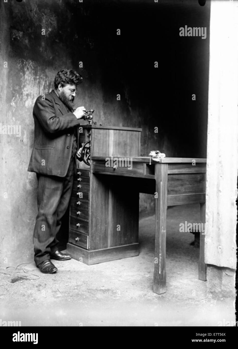 Foto von Magnús Benjamínsson, einem Uhrenforscher aus Reykjavik, Island, aufgenommen zwischen 1910 und 1920. Das Bild zeigt, wie er an einer Drehmaschine arbeitet, einem Werkzeug, das in der Uhrmacherei verwendet wird, mit seinem fokussierten Ausdruck und seinem unverwechselbaren Bart. Stockfoto