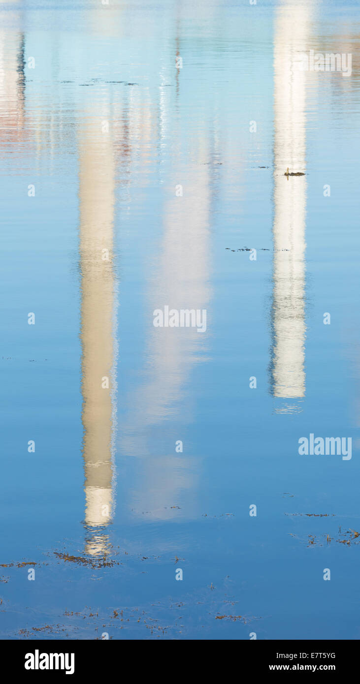 Die verschwommene Reflexion von zwei großen Schornsteine auf Salzwasser mit Algen Schwimmen im Vordergrund. Stockfoto