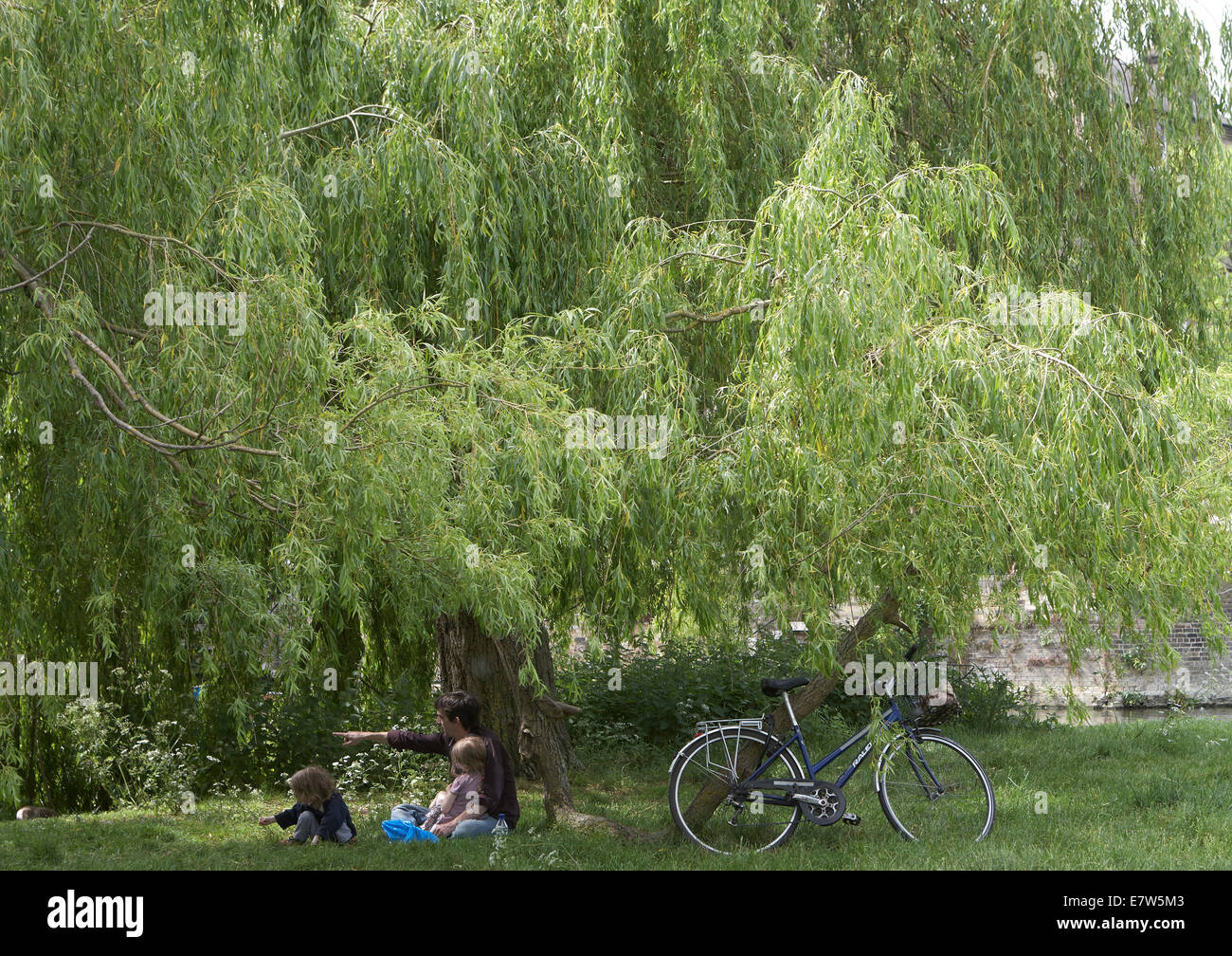 Mann sitzt mit Kindern am Flussufer mit Fahrrad Stockfoto