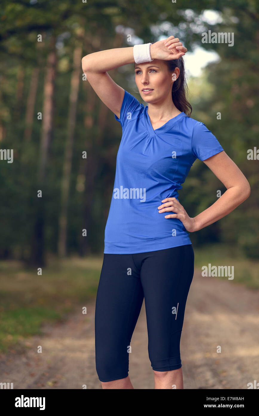 Sportlerin, Schweiß von der Stirn auf ihrem Armband abwischen, da sie während ihrer Übungen auf einem Waldweg macht eine Pause Stockfoto