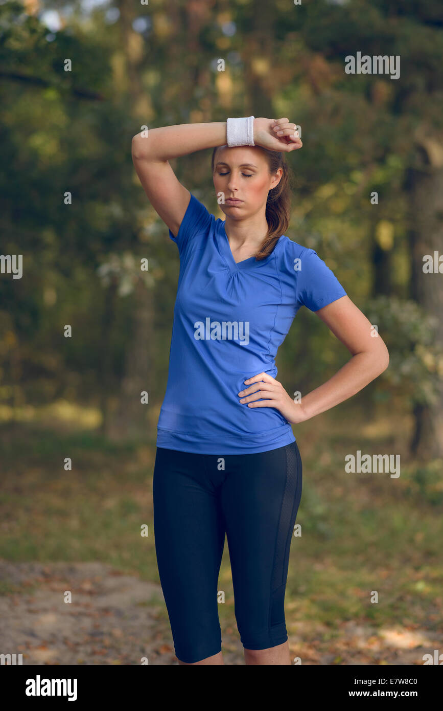 Sportlerin, Schweiß von der Stirn auf ihrem Armband abwischen, da sie während ihrer Übungen auf einem Waldweg macht eine Pause Stockfoto