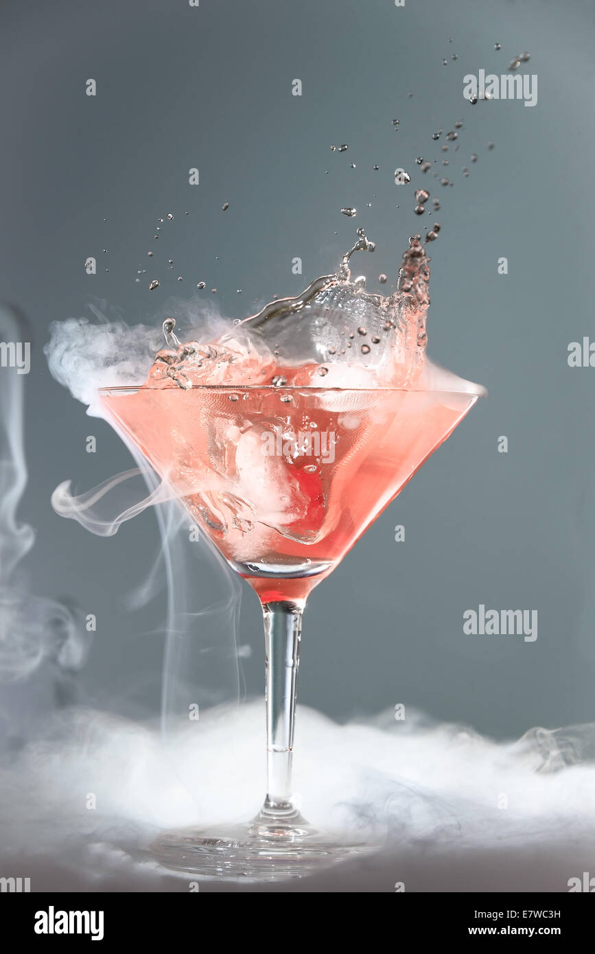 Rauchen Martini cocktail in einem konischen Glas mit wabernden Dampf und Spritzwasser Tropfen aus einer fallenden Kirsche für eine dramatische effe Stockfoto