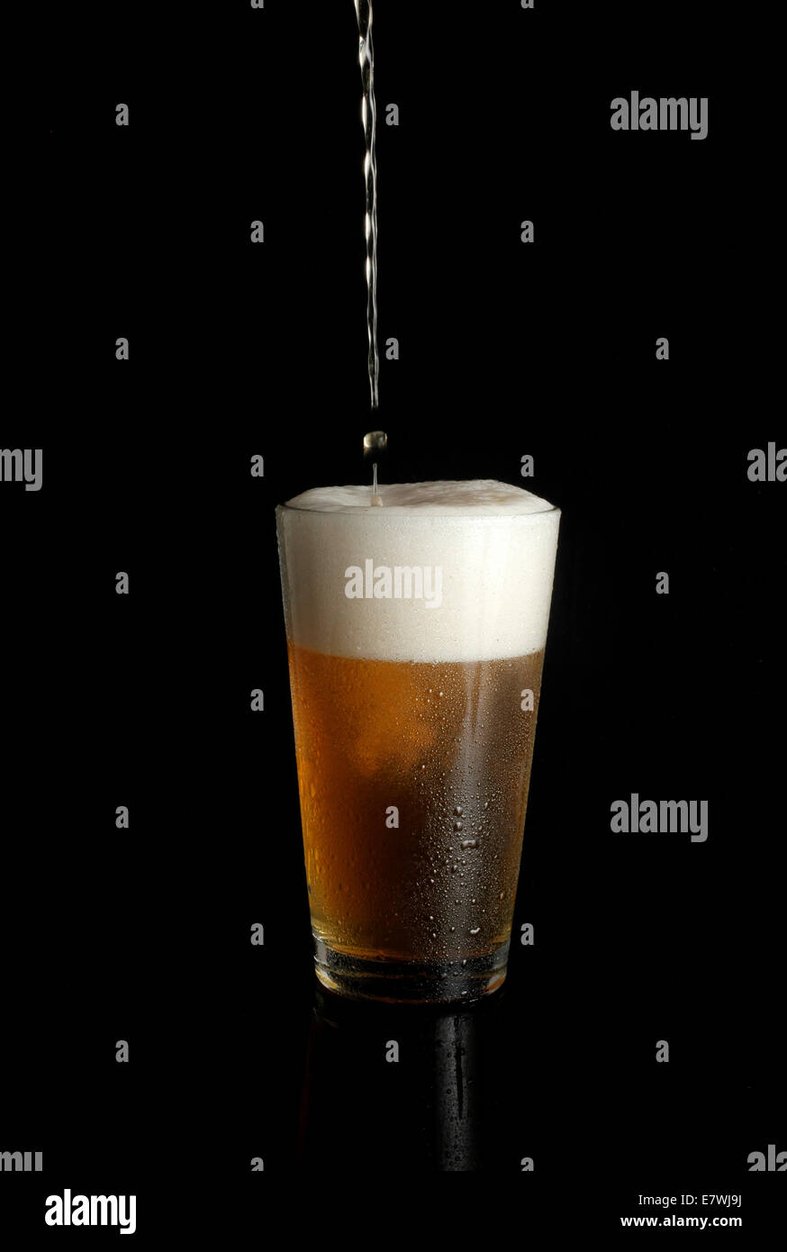 Unbeschriftetes Bier wird in Pint Glas auf schwarzem Hintergrund gegossen Stockfoto