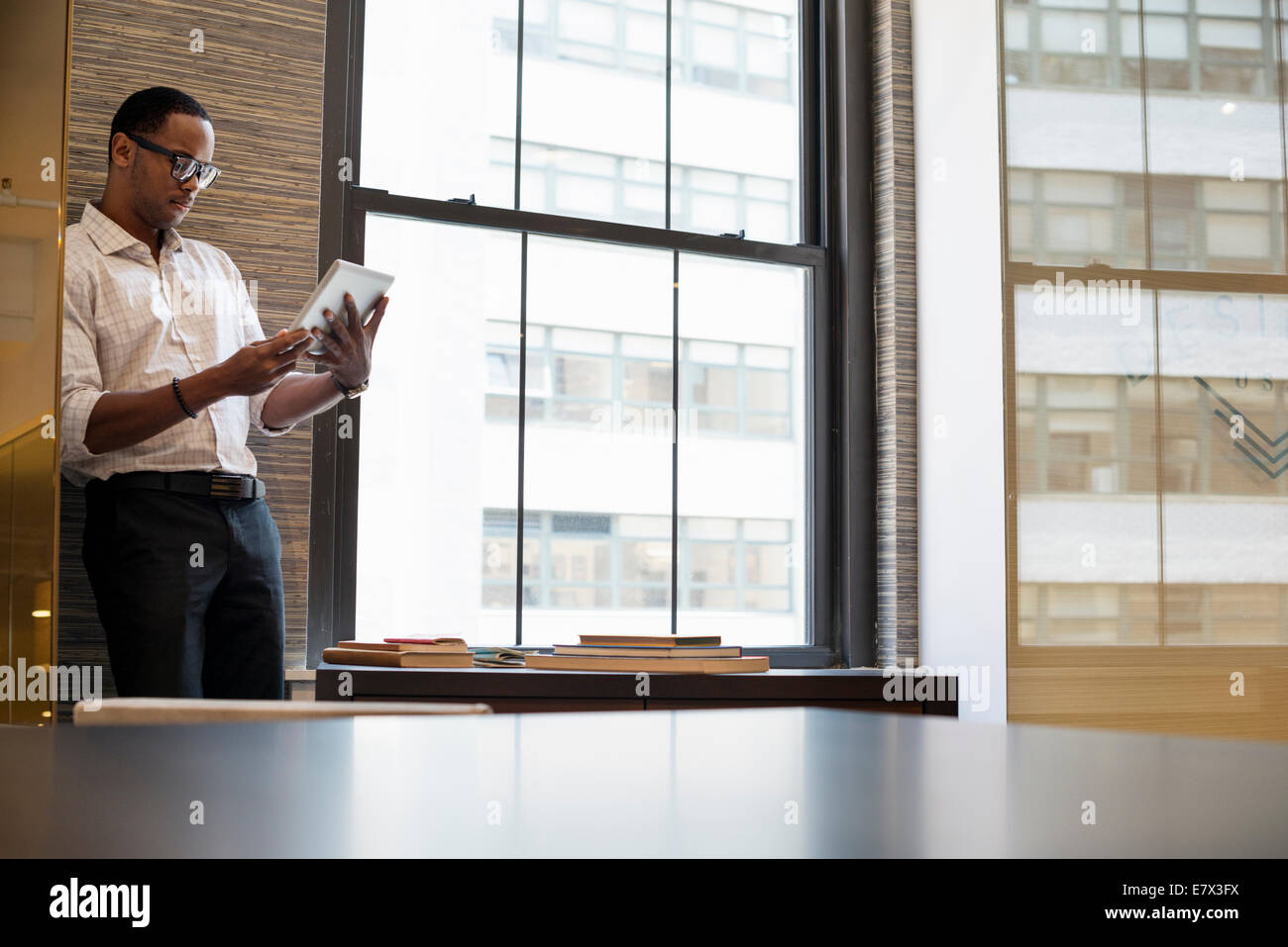 Ein Mann, der durch ein Fenster in einem Büro mit einem digitalen Tablet. Stockfoto