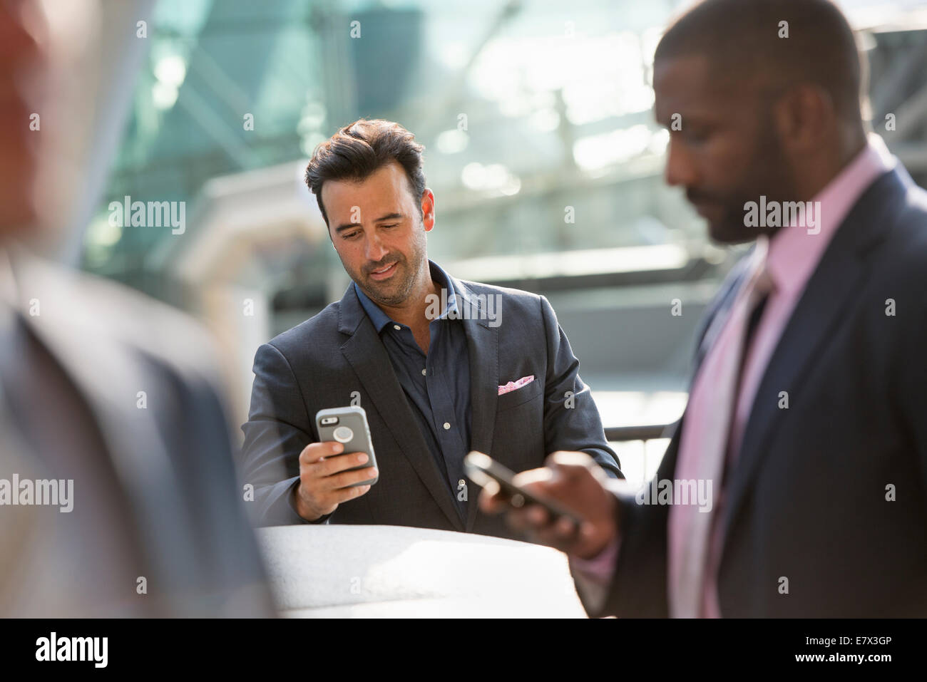 Eine Gruppe von drei Geschäftsleute, zwei überprüfen ihre Telefone. Stockfoto