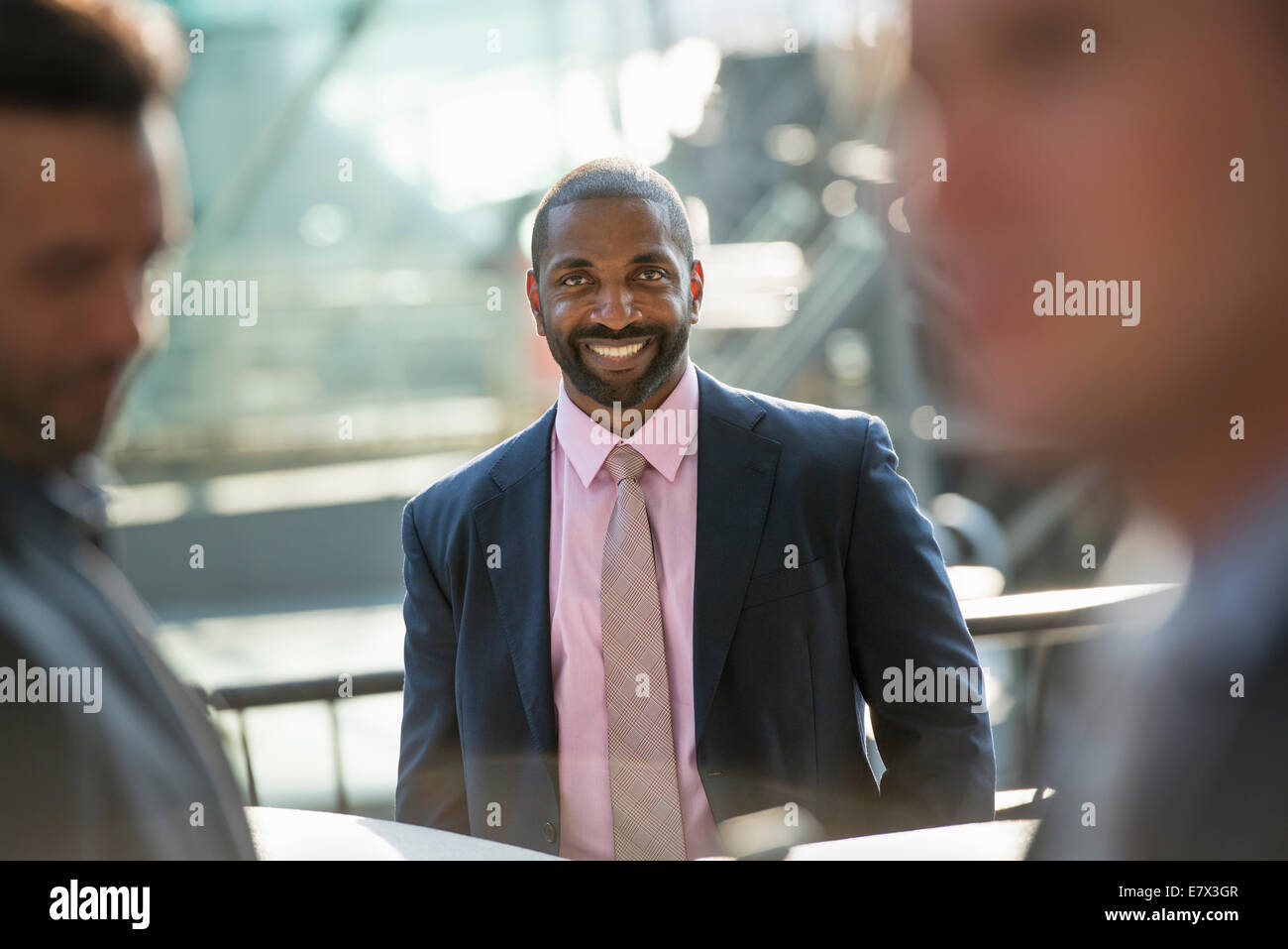 Ein Business-Mann sitzt lächelnd souverän, in einer Gruppe mit zwei anderen. Stockfoto