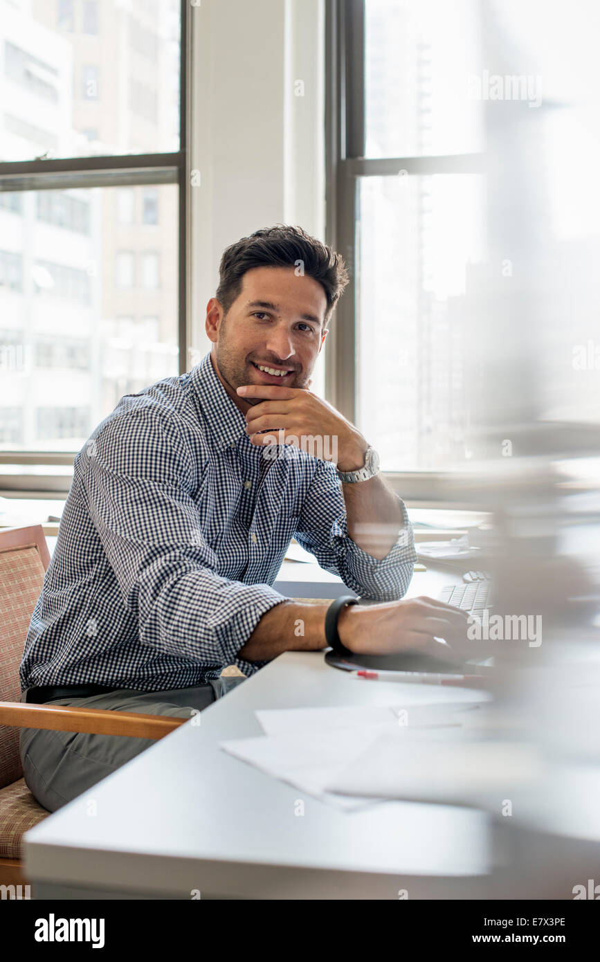 Büroalltag. Ein Mann sitzt an einem Schreibtisch in die Kamera schaut. Stockfoto