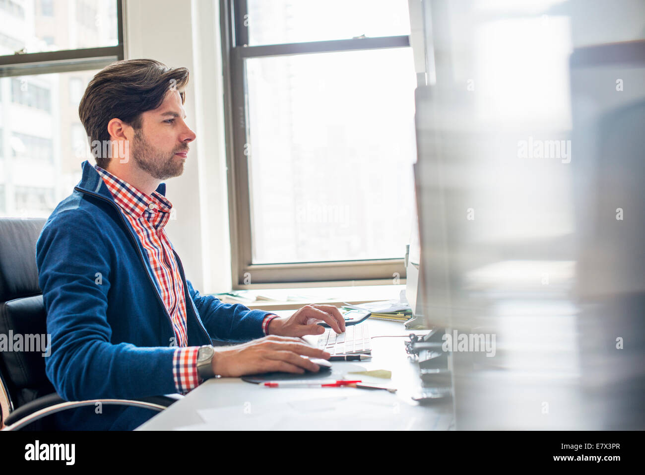 Büroalltag. Ein Mann sitzt an einem Schreibtisch mit einem Computer Blick unverwandt auf dem Bildschirm. Stockfoto