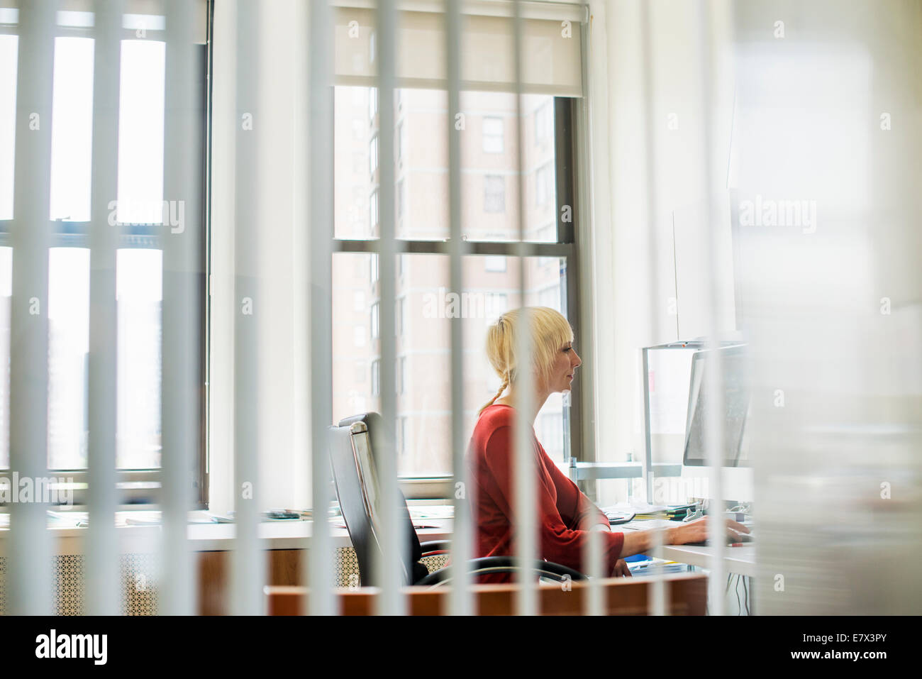 Büroalltag. Eine Frau sitzt an einem Schreibtisch mit einem Computer Blick unverwandt auf dem Bildschirm. Stockfoto