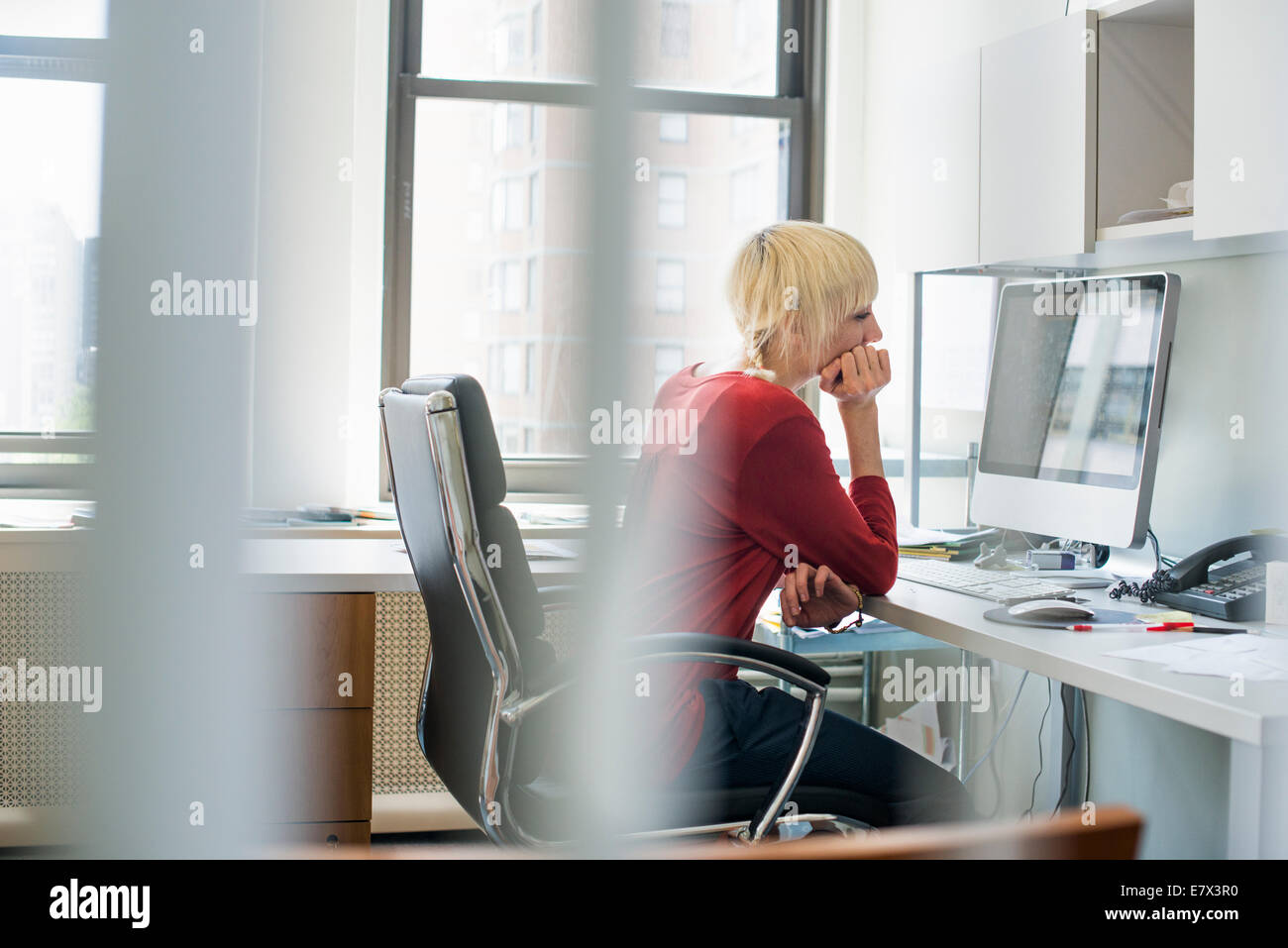 Büroalltag. Eine Frau sitzt an einem Schreibtisch mit einem Computer Blick unverwandt auf dem Bildschirm. Stockfoto