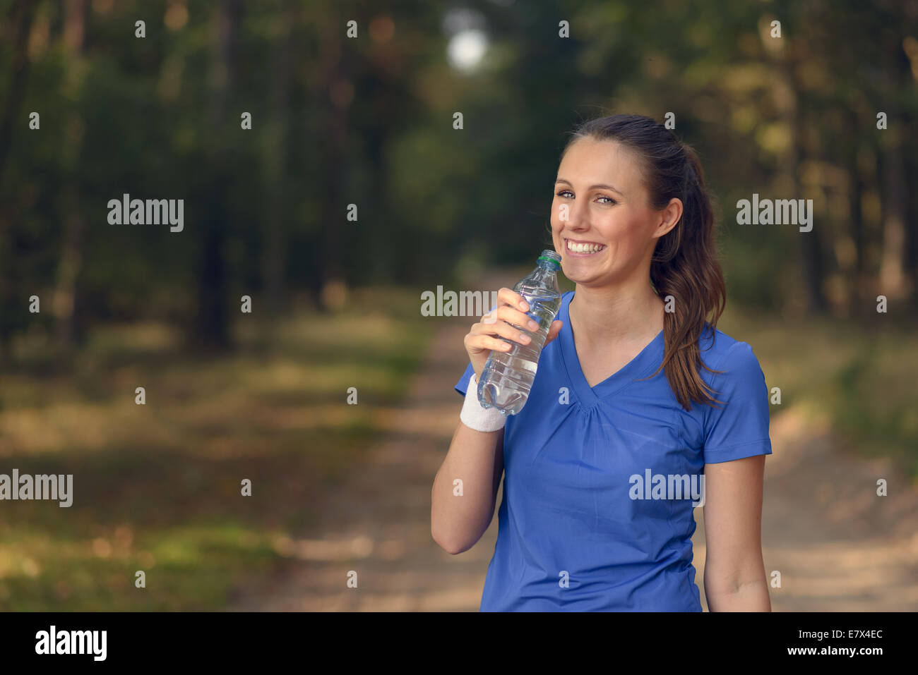 Schlanke junge Frau in Sportkleidung, abgefülltes Wasser zu trinken, wie sie auf einen Waldweg, bei einem Trainingslauf Re-Hydrat hält fit Stockfoto