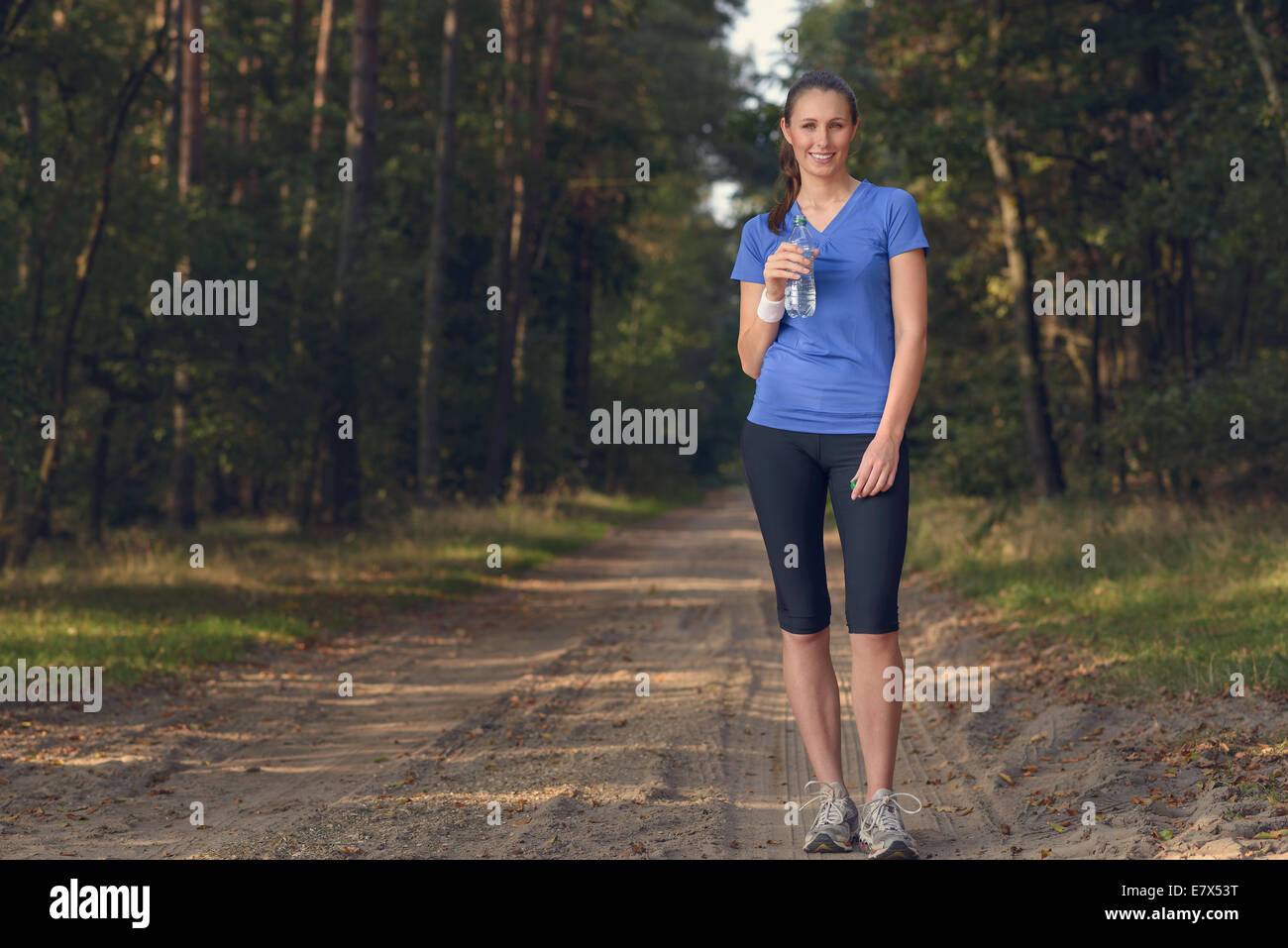 Schlanke junge Frau in Sportkleidung, abgefülltes Wasser zu trinken, wie sie auf einen Waldweg, bei einem Trainingslauf Re-Hydrat hält fit Stockfoto