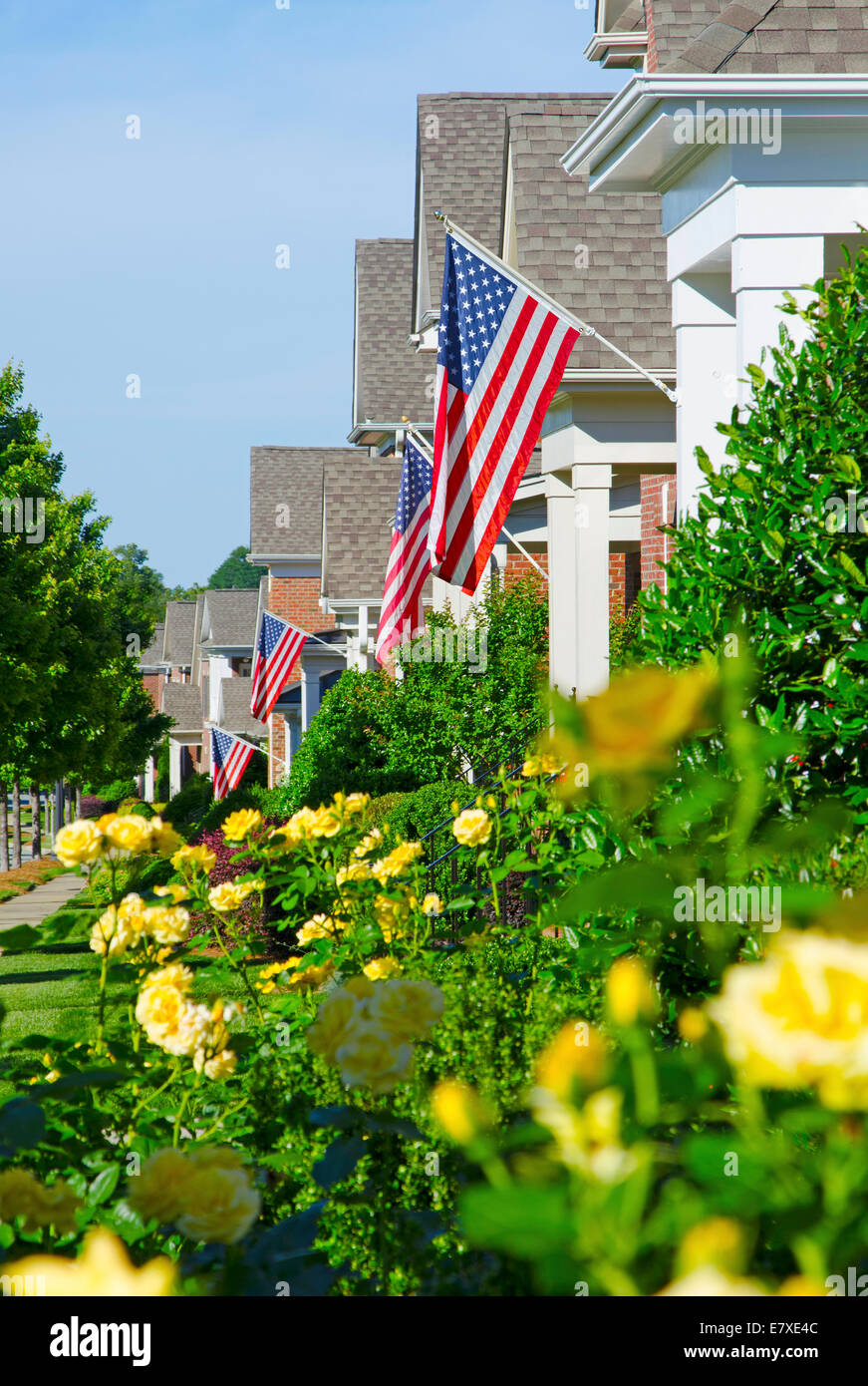 Amerikanische Flaggen hängen von einer vorderen Veranden in einem Viertel von hochwertigen, Ziegel Häuser anlässlich des bevorstehenden Urlaub. Stockfoto