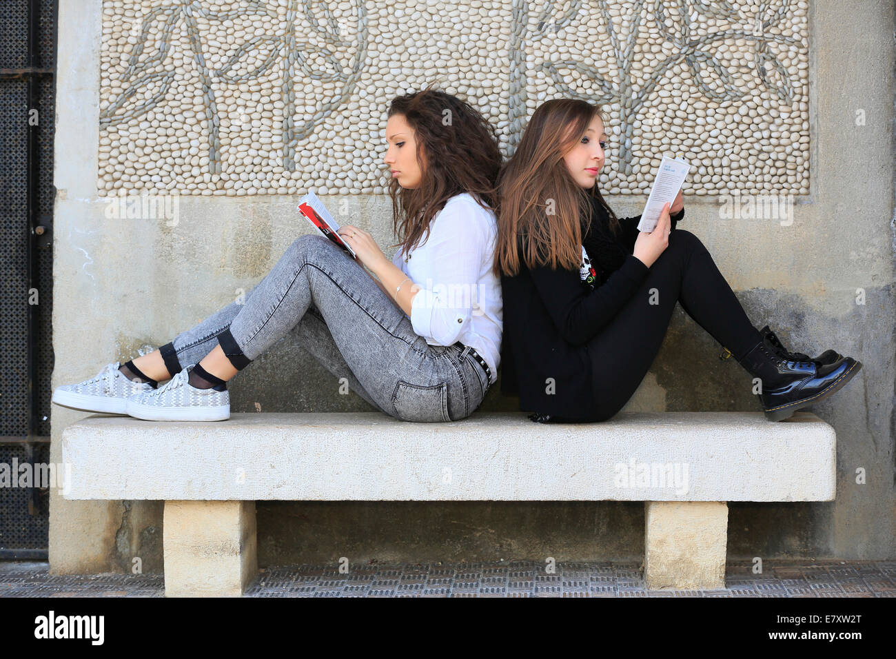 Zwei Freundinnen, Teenager, sitzen Rücken an Rücken auf einer Steinbank, Lesebücher, Menton, Alpes-Maritimes, Provence-Alpes Stockfoto