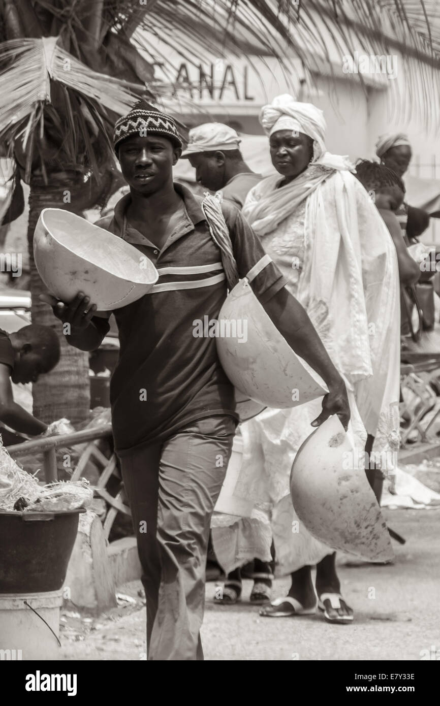 Mbour, Senegal - Juli 2014: Ein Mann trägt große Schüsseln auf den Straßenmärkten am 9. Juli 2014 in Mbour, Senegal zu verkaufen. Stockfoto