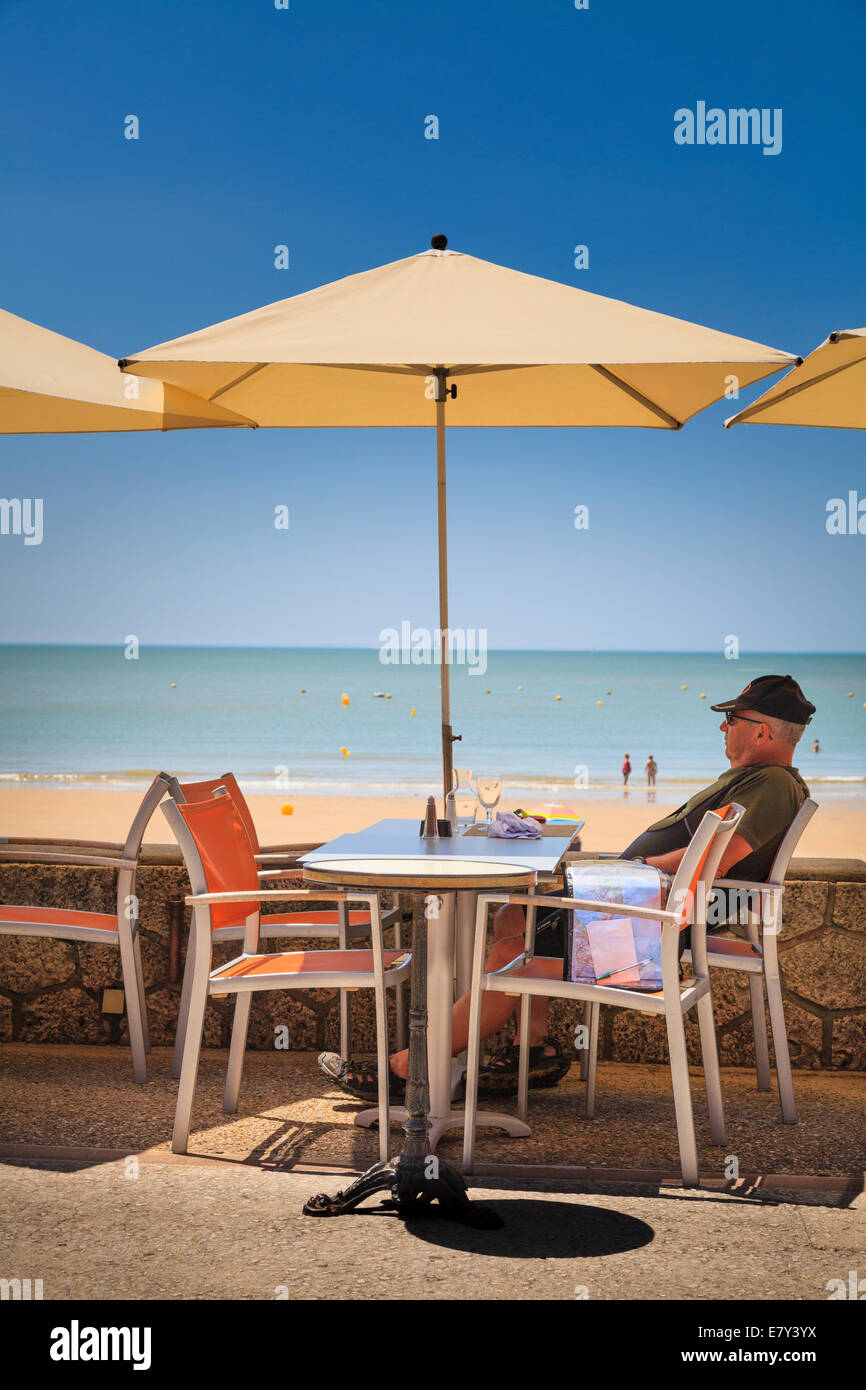 Ein Mann sitzt unter Dach am Café-Tisch von Strand. Stockfoto
