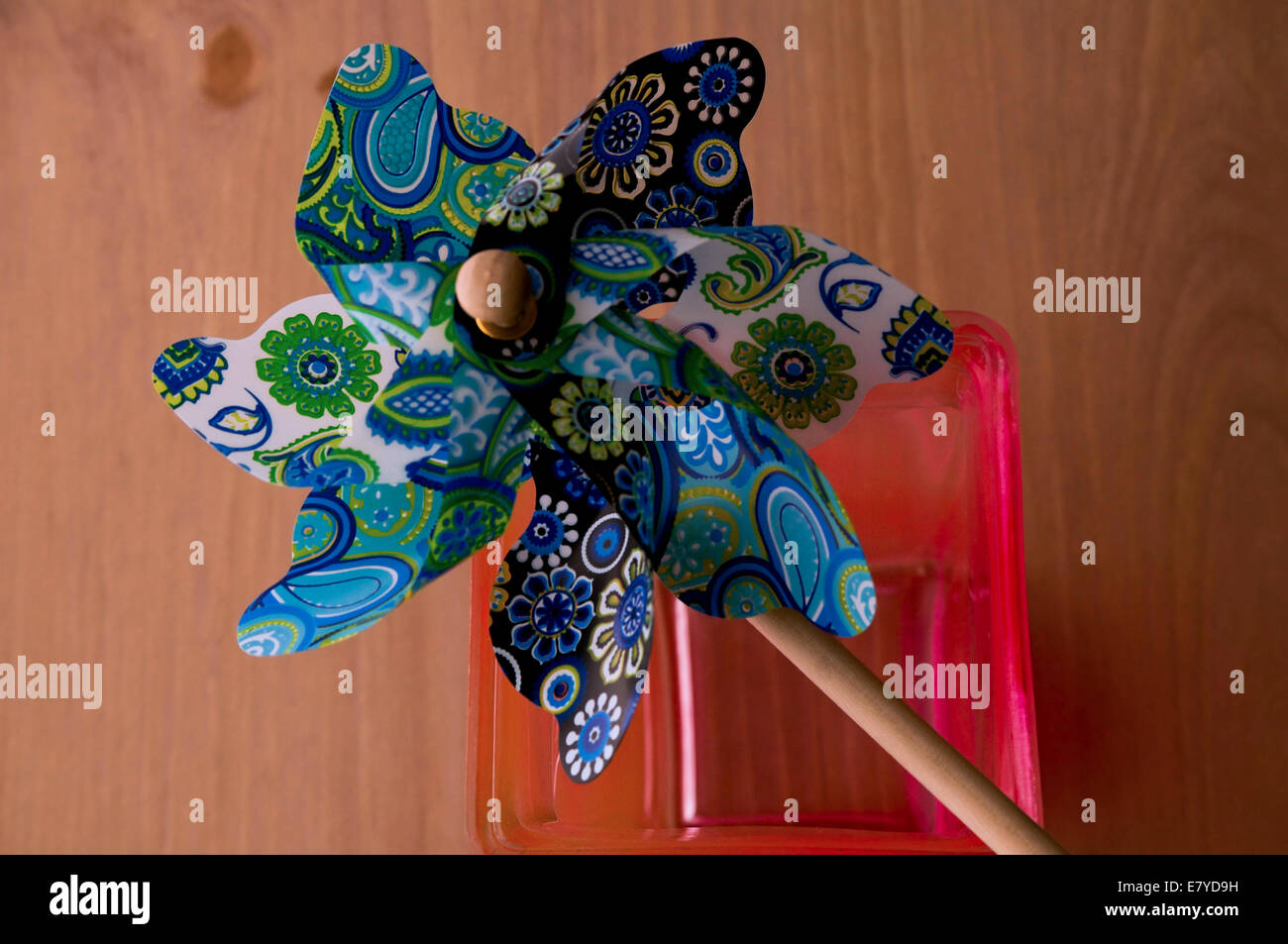 Bunte blau, grün, gelb, weiß und schwarz Windrad Verlegung auf eine rosa Vase auf einem Holztisch Hintergrund Stockfoto