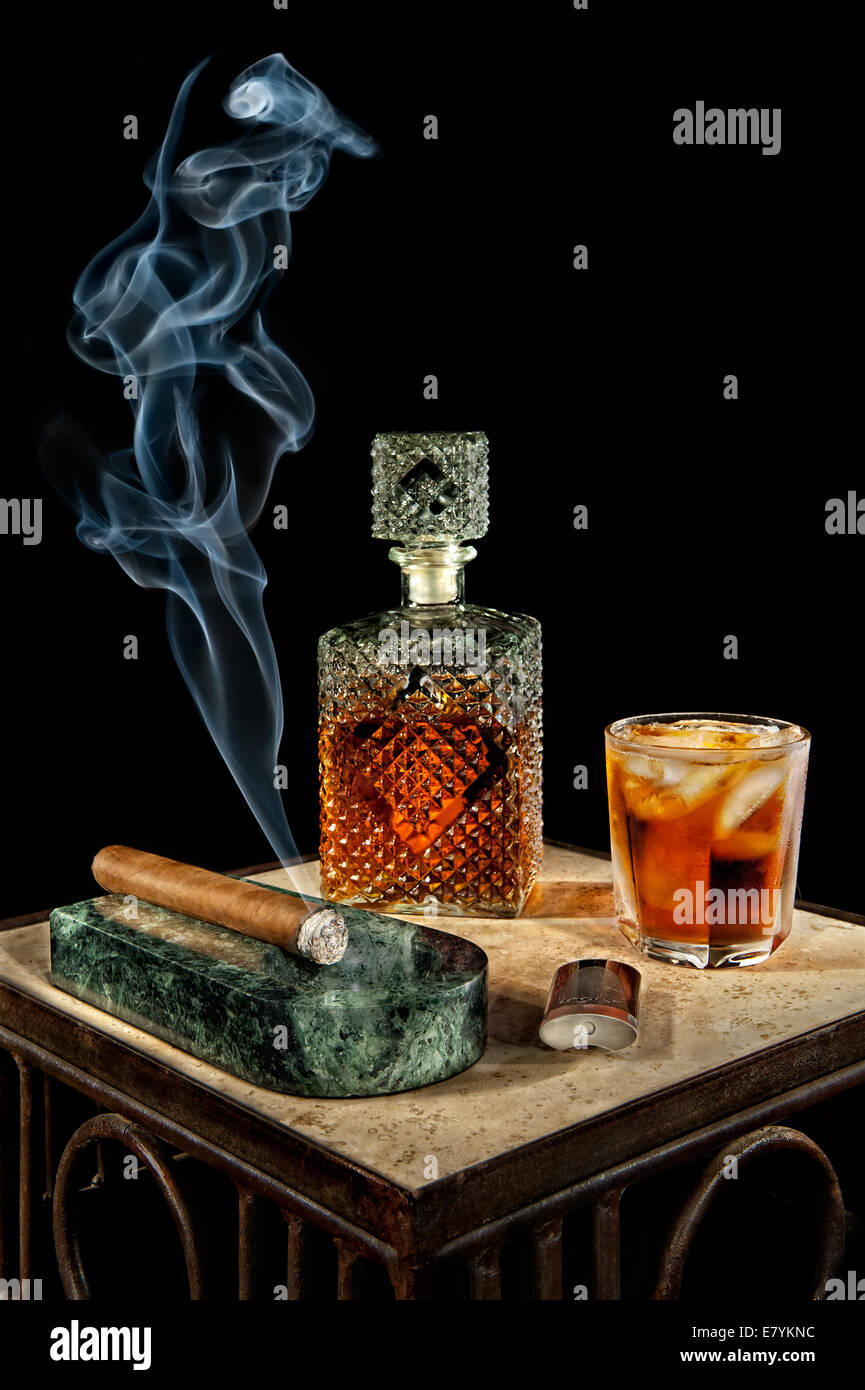 Eine Zigarre rauchen setzt neben einer Kristallkaraffe von Alkohol. Stockfoto