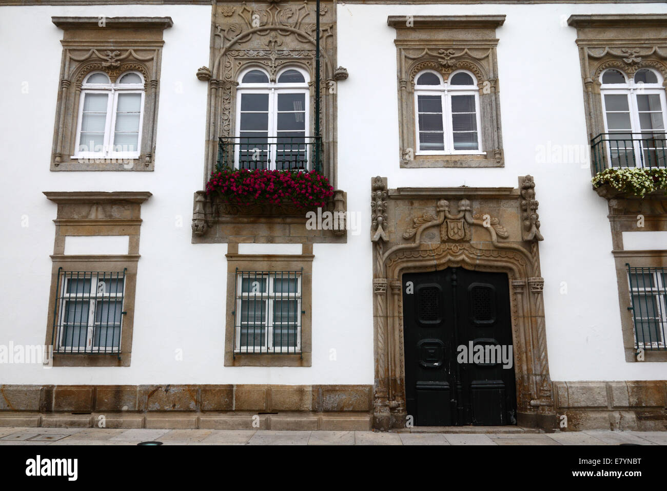 Reich geschnitzte Steintür und Fenster der Fassade der Villa Casa de Carreira mit Geranien in der Fensterbox, Viana do Castelo, Nord-Portugal Stockfoto