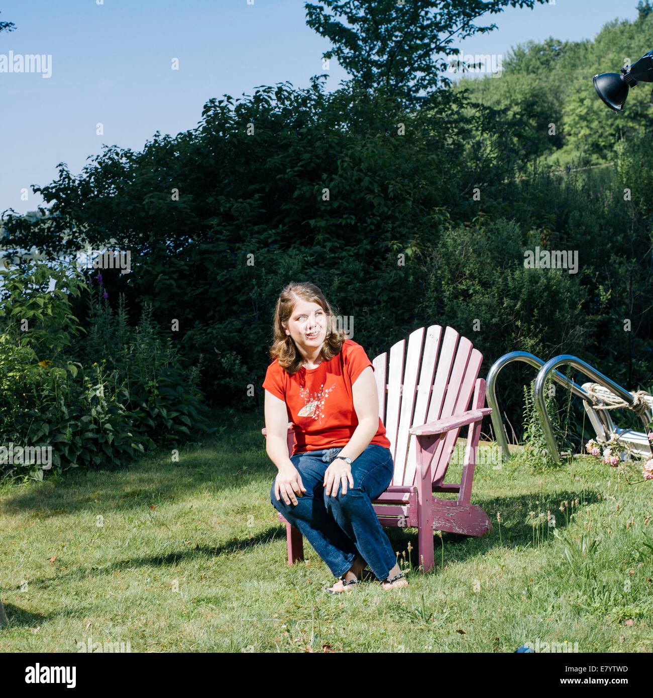 Frau sitzt am Rand der Holzstuhl auf Rasen Stockfoto