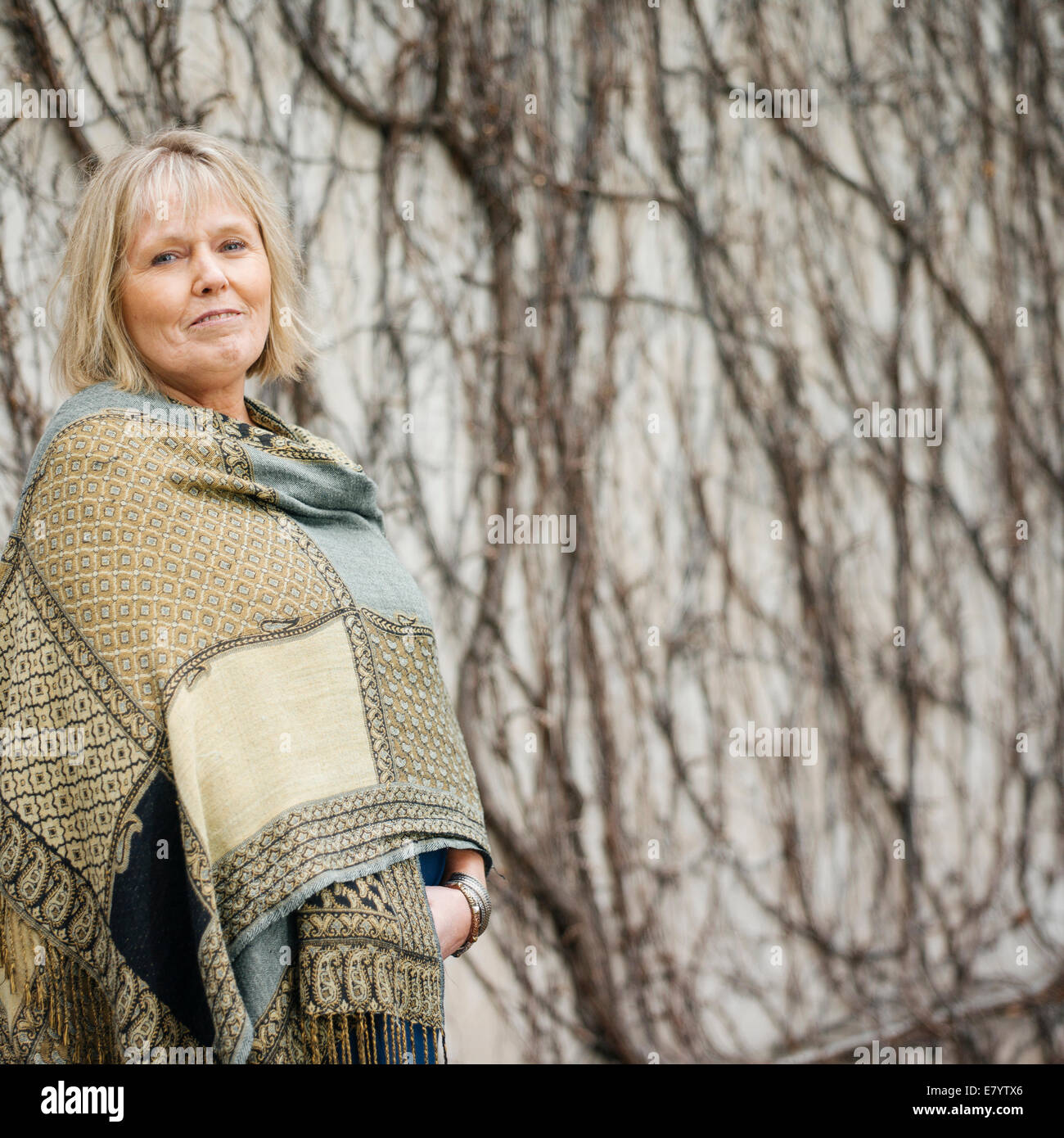 Ältere Frau im Schal stehen gegen die Wand bedeckt in blattlosen Efeu Stockfoto