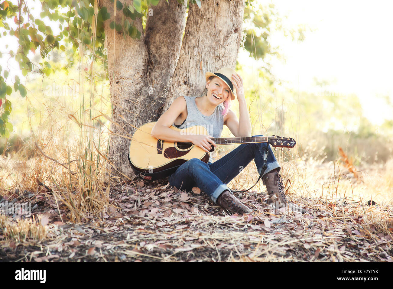 Frau mit Akustikgitarre sitzen unter Baum Stockfoto