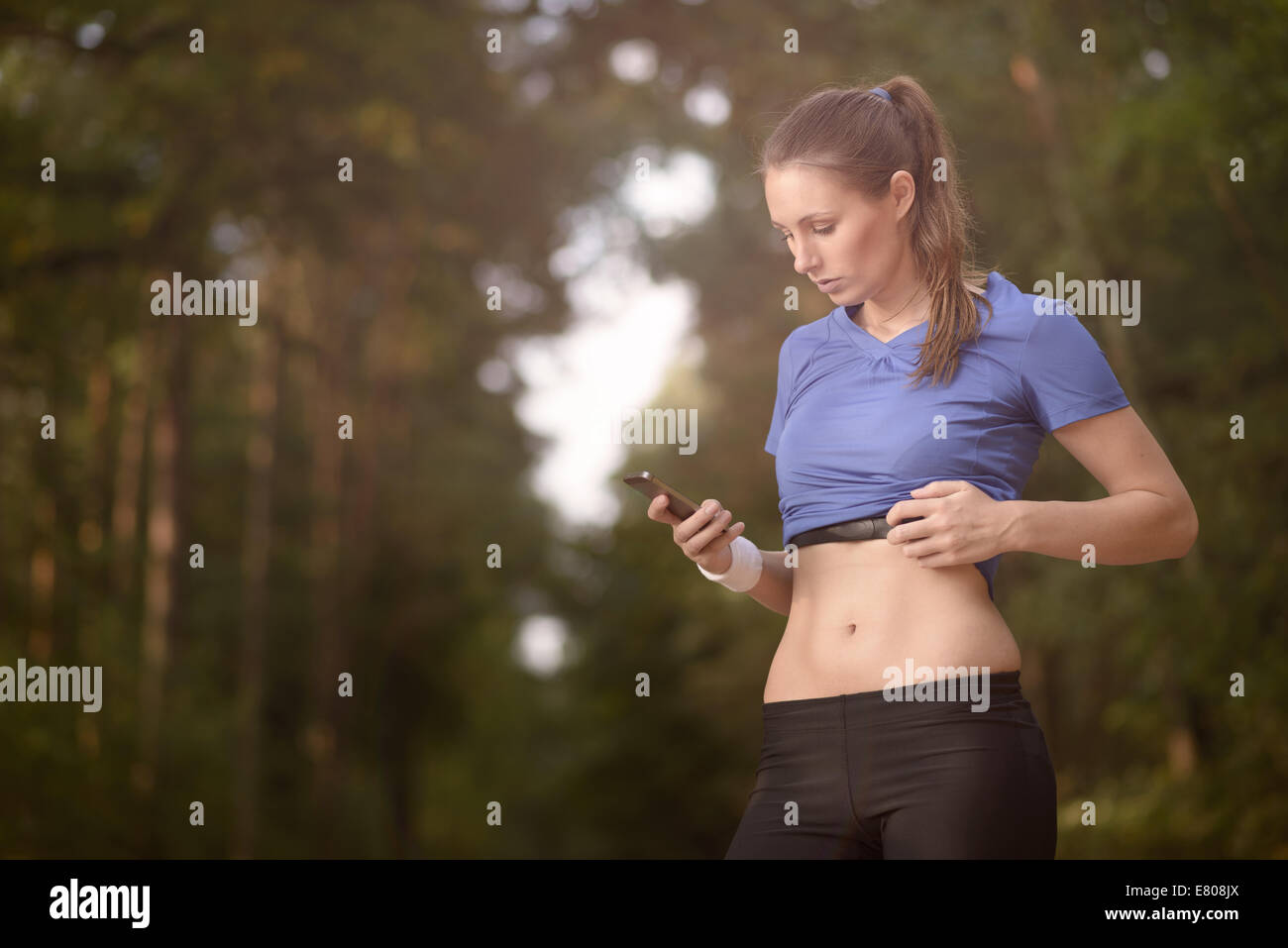 Junge sportliche Frau trainieren im Wald stehen, die ihr Smartphone zu betrachten, wie sie eine mobile Anwendung elektronischer nutzt Stockfoto