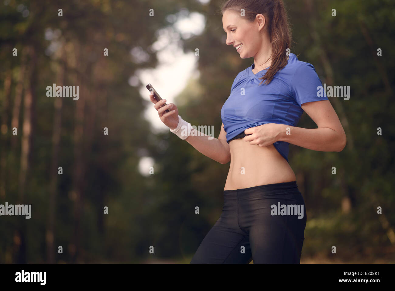 Junge sportliche Frau trainieren im Wald stehen, die ihr Smartphone zu betrachten, wie sie eine mobile Anwendung elektronischer nutzt Stockfoto