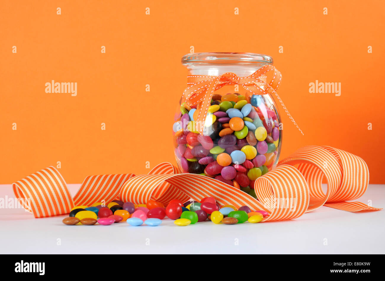 Candy in Glas mit orangefarbenen und weißen Streifen Band für Halloween oder Partei begünstigt. Stockfoto