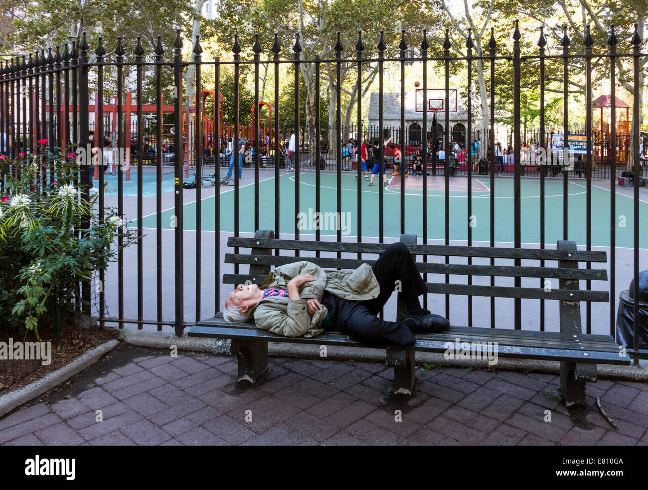 Senior asiatischen Mann auf Bank schlafen, während die asiatischen Kinder spielen Basketball in New York Columbus Park in Chinatown Stockfoto