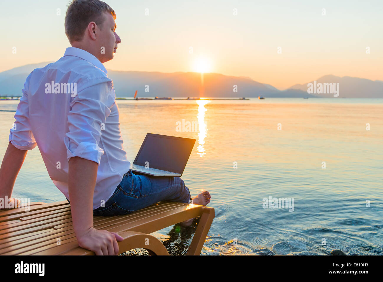 ein junger Mann auf einer Sonnenliege am Wasser Stockfoto