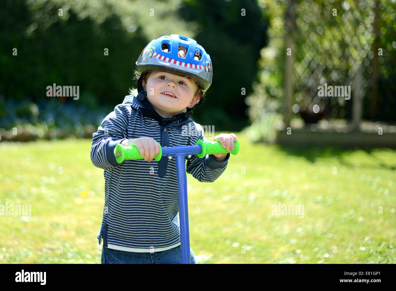 Zwei Jahre alter Junge spielt auf seinem Roller in einen Garten, einen Helm zu tragen Stockfoto