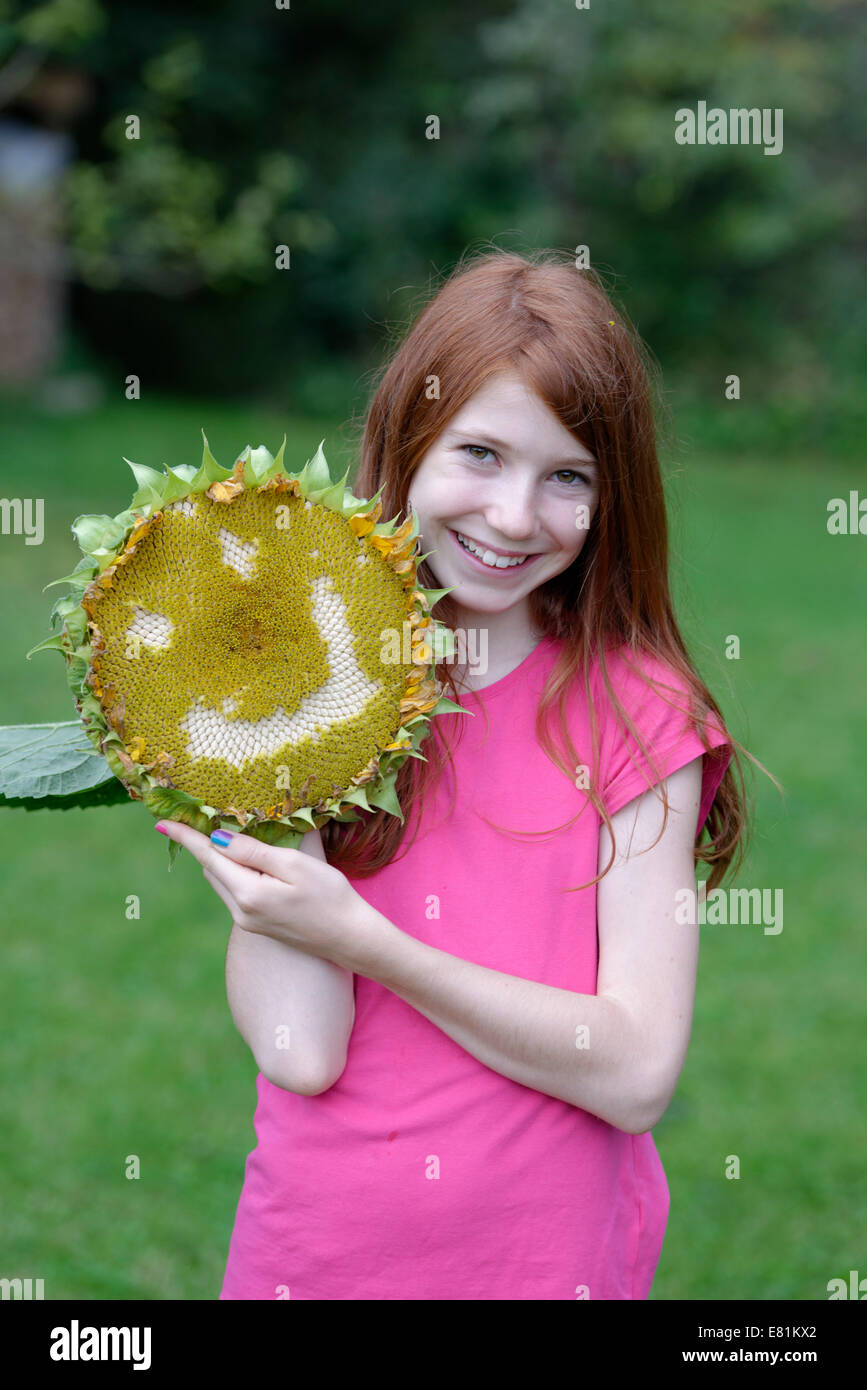 Mädchen hält eine Sonnenblume (Helianthus Annuus) mit einem lächelnden Gesicht Stockfoto