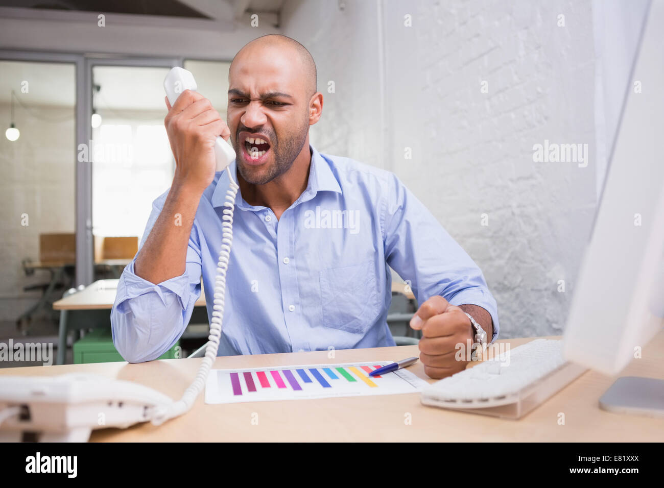 Wütend Geschäftsmann mit Telefon am Schreibtisch Stockfoto