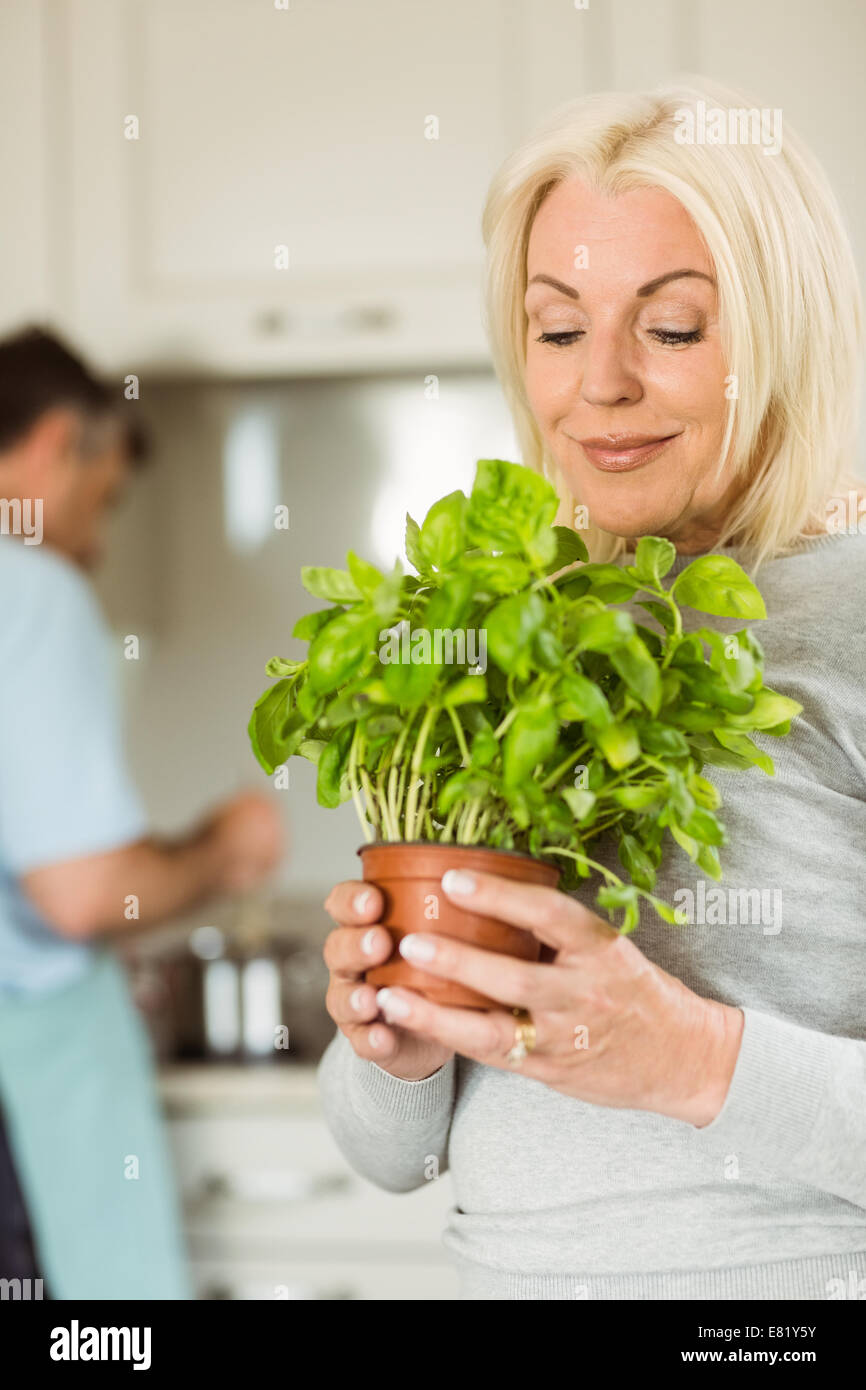 Reife blonde lächelnde und riecht ihr Basilikum Pflanze Stockfoto