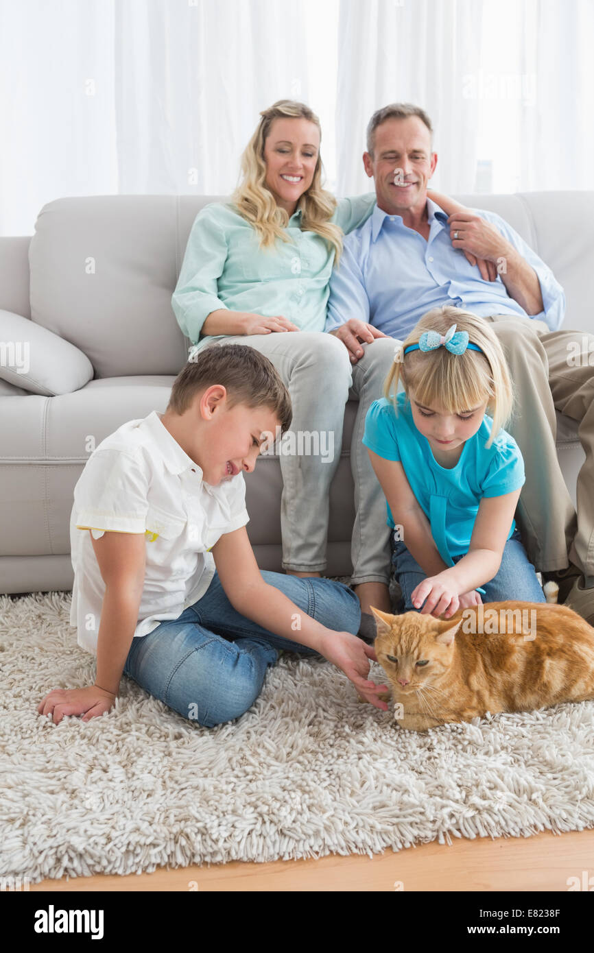 Lächelnde Familie mit ihrer Ingwer Katze auf dem Teppich Stockfoto