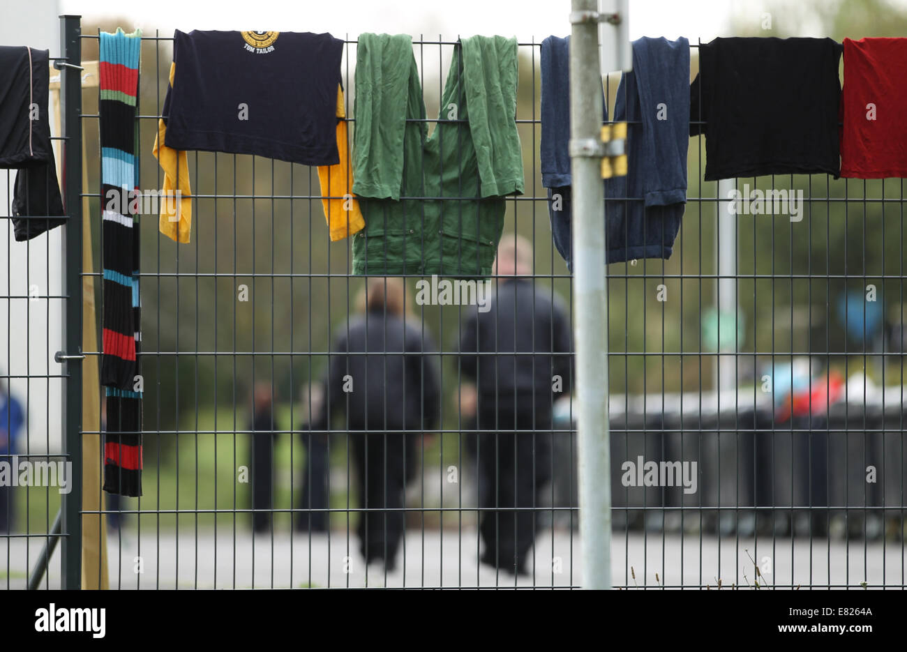 Burbach, Deutschland. 29. Sep, 2014. Sicherheitspersonal (Hintergrund) ist zu Fuß auf der Website von einem Flüchtlingsheim in der ehemaligen Siegerland-Kaserne während Wäsche von einem Zaun in Burbach, Deutschland, 29. September 2014 hängt abgebildet., privates Sicherheitspersonal hat angeblich verletzt und angegriffene Menschen Asyl in einem Flüchtlingslager in Burbach zu Hause. Die ehemalige Siegerland Baracken dient als ein Notunterkünfte für Flüchtlinge und Asylsuchenden Menschen. Bildnachweis: Dpa picture Alliance/Alamy Live News Stockfoto