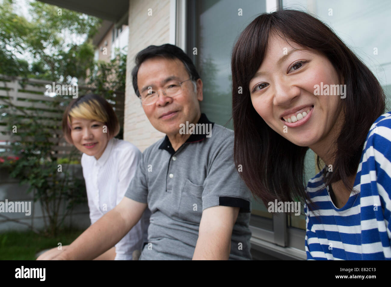 Ein Mann und zwei Frauen sitzen zu Hause im Garten. Ein Vater und zwei Töchter. Stockfoto
