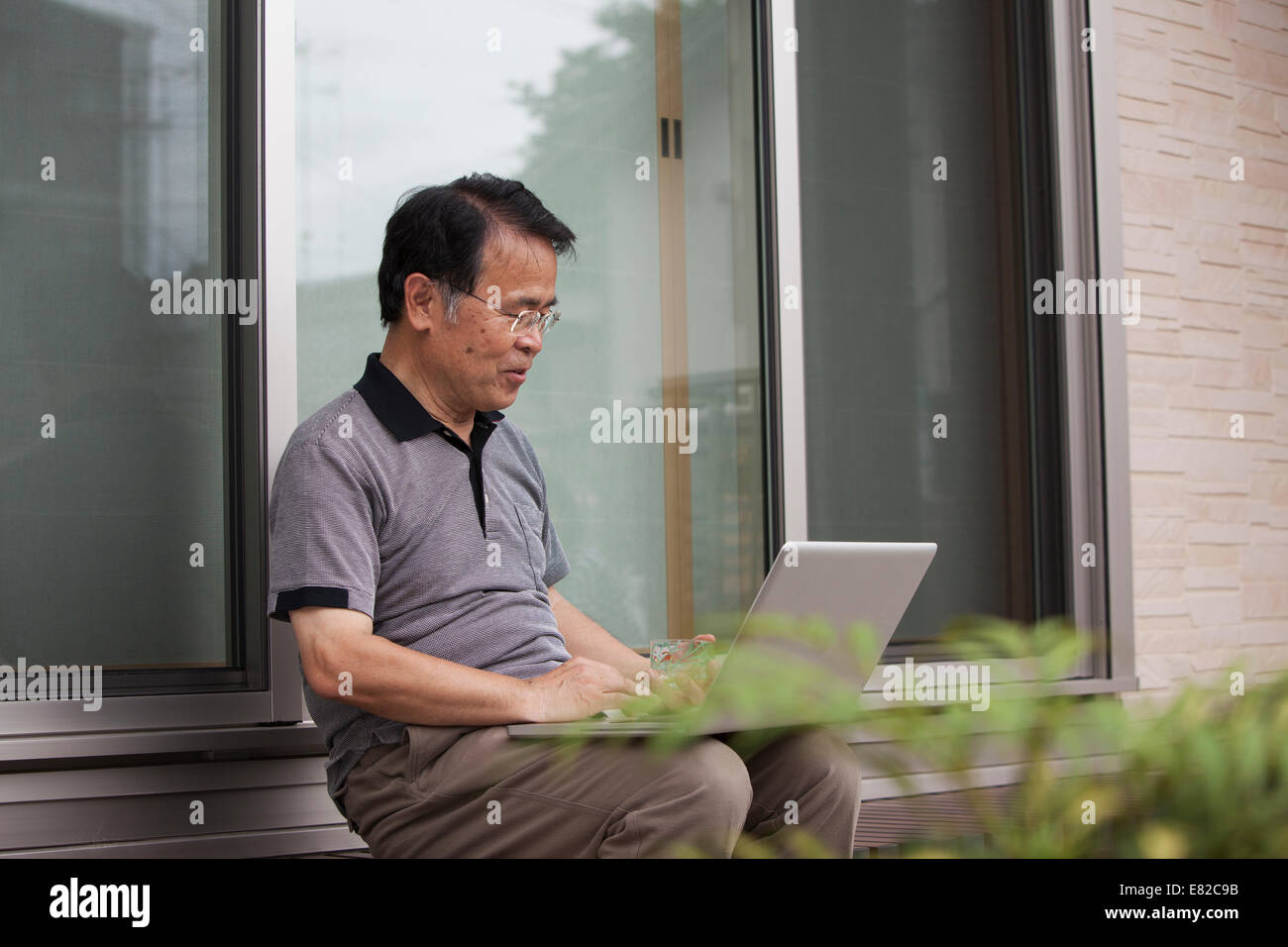 Ein Mann sitzt vor einem Haus. Halten einen Laptop-Computer. Stockfoto