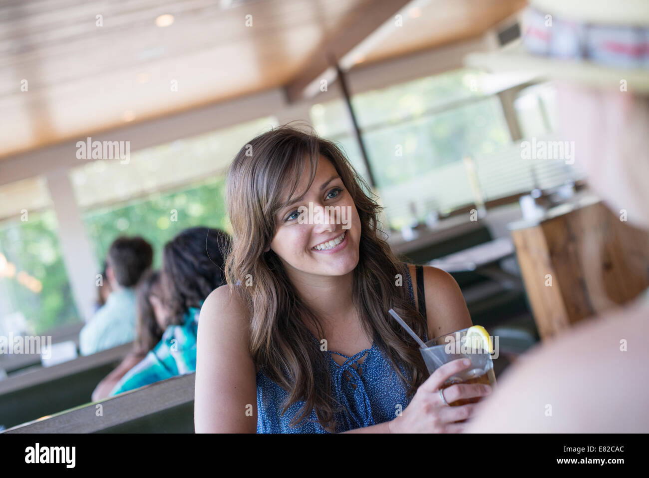Eine junge Frau sitzt an einem Tisch in einem Diner mit einem kühlen Getränk. Stockfoto